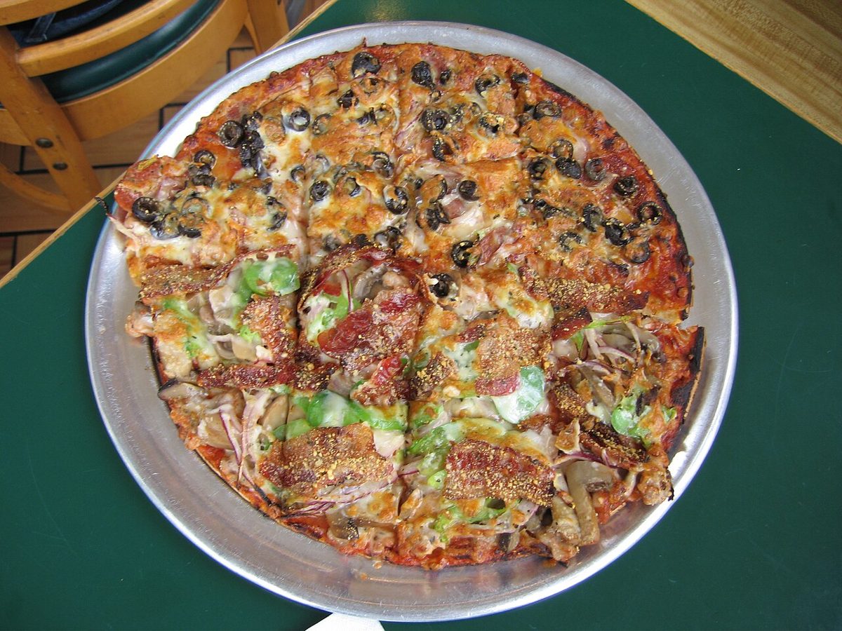 A thin-crust, square-cut pizza topped with black olives, mushrooms, green peppers and bacon on a metal tray at an Imo's in St. Louis