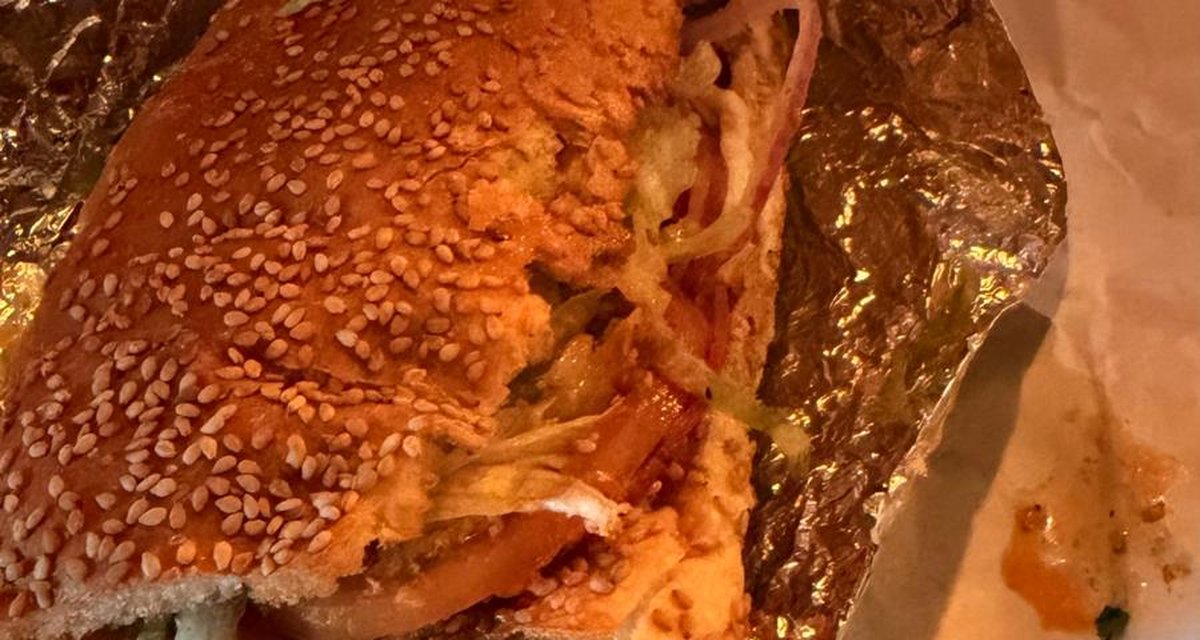 A sesame-seed baguette sandwich wrapped in foil and paper